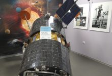 A communications satellite orbiting Earth with solar panels extended above the planet's curved horizon.